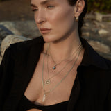 Close-up of model wearing the Balance Crystal Charm in Clear Quartz layered with gold pendant necklaces.