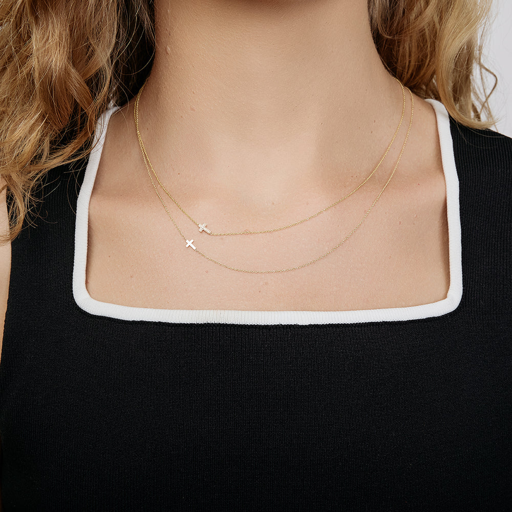 Close-up of a person wearing a delicate gold necklace with a small gold cross charm.