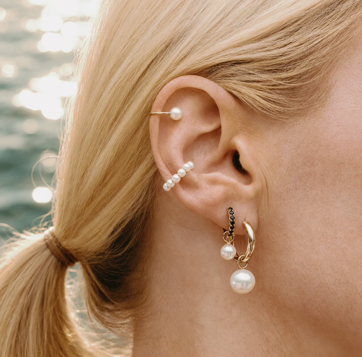 Model wearing Maya Brenner Halo Pearl Ear Cuff styled in an ear stack with pearl earring charms on gold hoop earrings