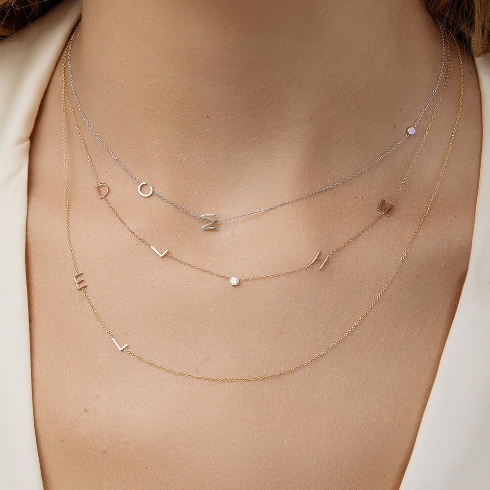 Layered initial necklaces on a model wearing a beige top