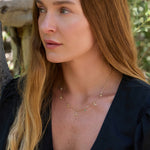 Woman wearing a gold Paris necklace with various pendants outdoors