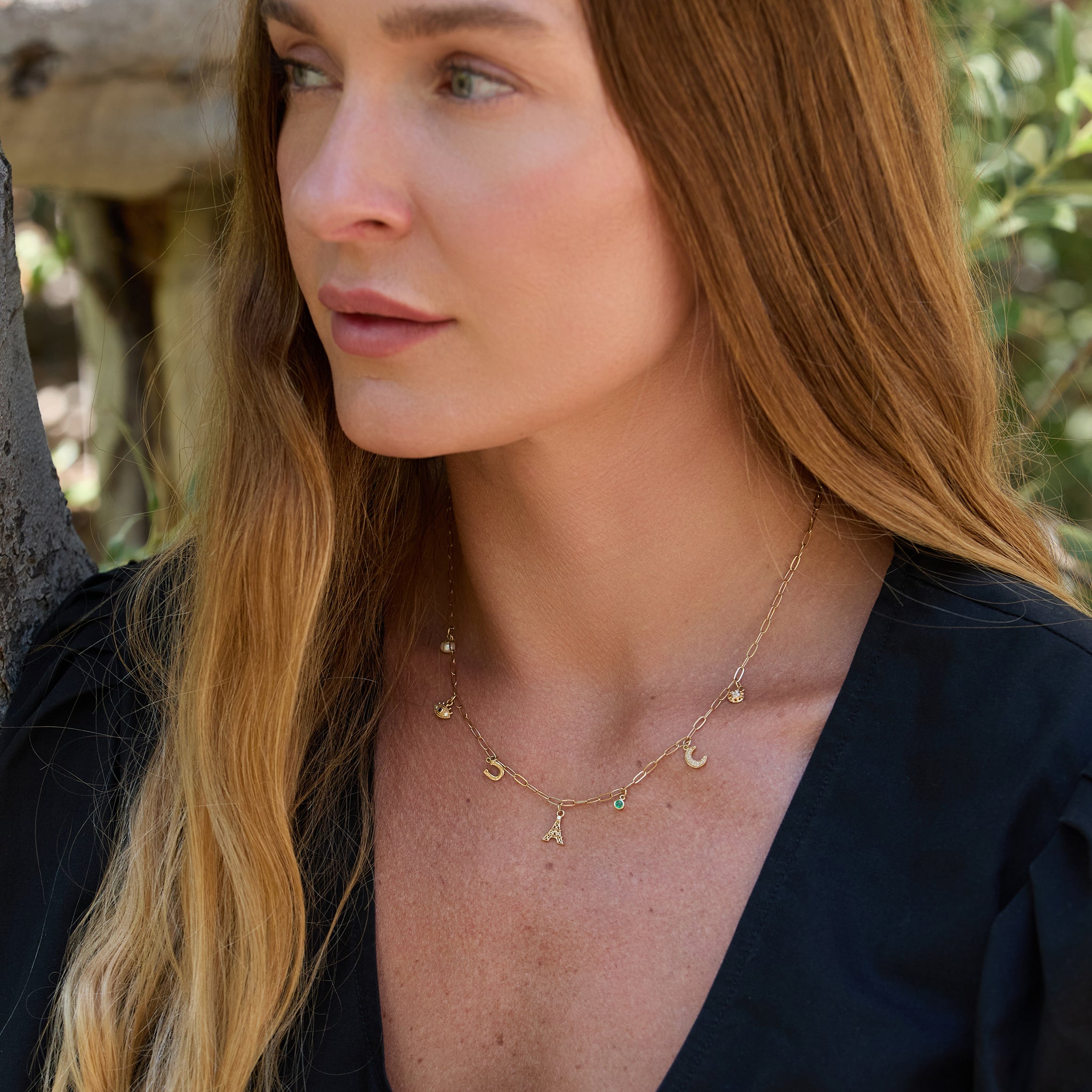 Woman wearing a gold Paris necklace with various pendants outdoors