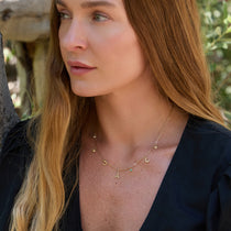 Woman wearing a gold Paris necklace with various pendants outdoors