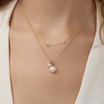 The Pavé Monogram Necklace with Diamond in Yellow Gold layered with a necklace that has a  pearl pendant on a model.