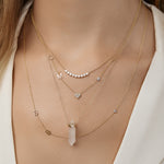 The Clarity Retreat Necklace layered with gold necklaces that have various charms on a person wearing a white shirt.