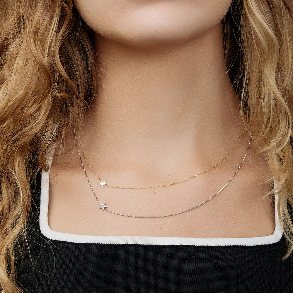 Close-up of a person wearing layered delicate gold necklaces, each with star charms.