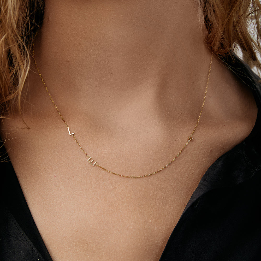 Gold necklace with small initials and a birthstone on a model wearing a black top.