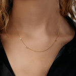 Gold necklace with small initials and a birthstone on a model wearing a black top.