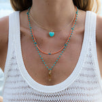 Model wearing the Turquoise Heart Charm on an Omega Chain with layered turquoise and coral necklaces.
