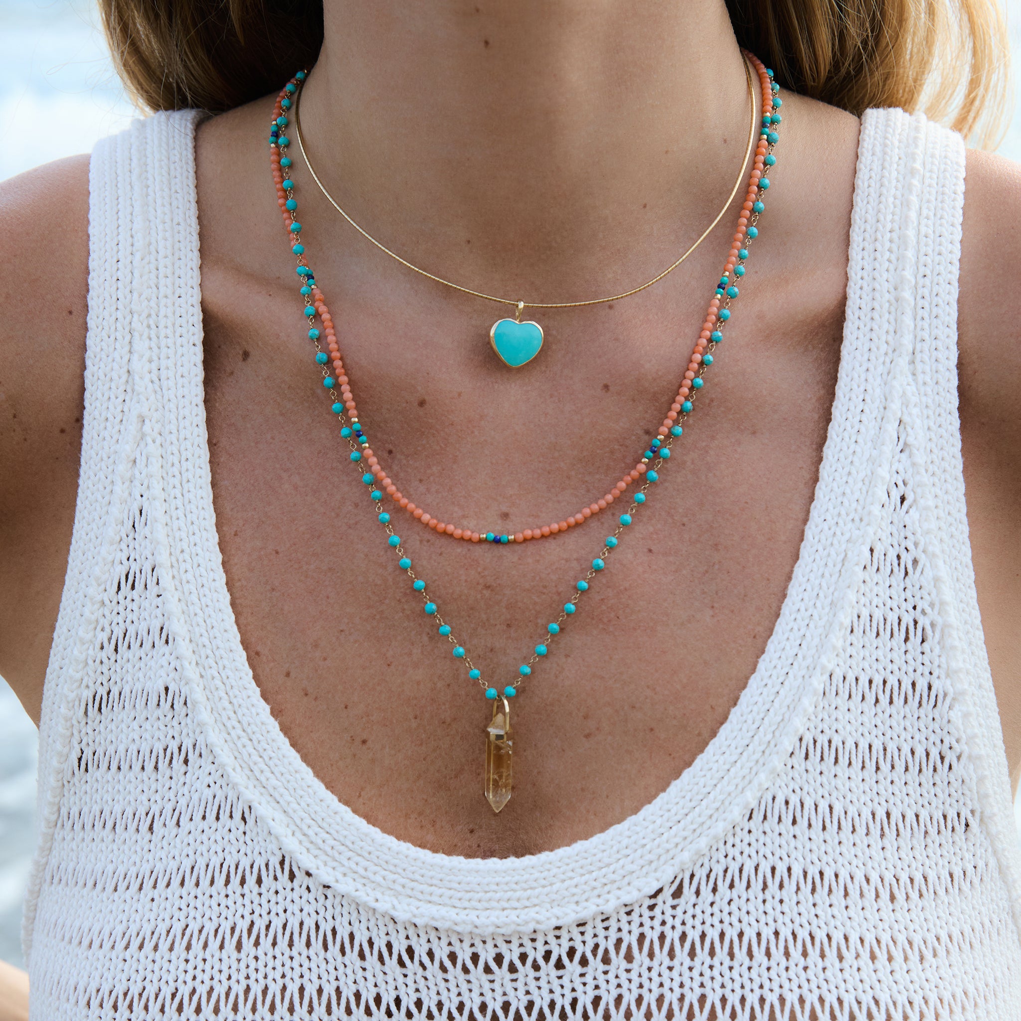 Model wearing the Turquoise Heart Charm on an Omega Chain with layered turquoise and coral necklaces.