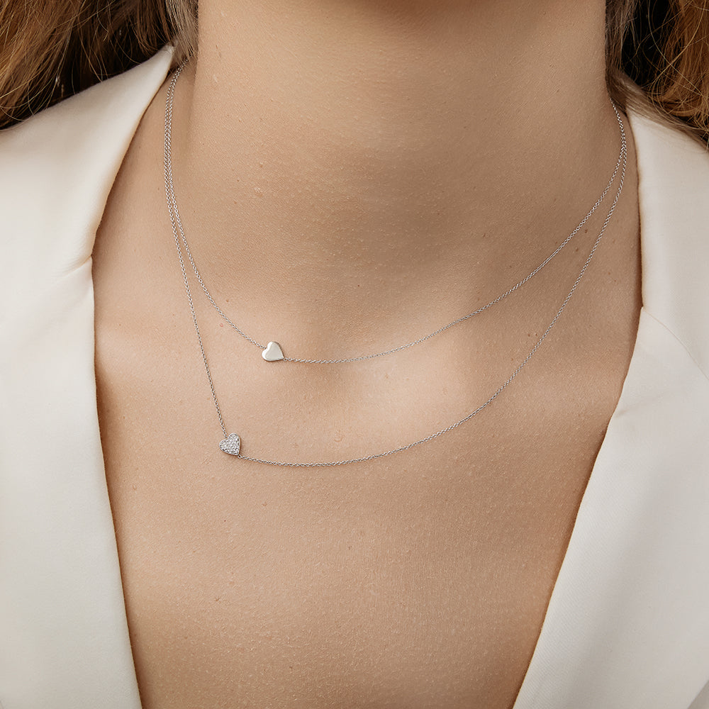 Two dainty white gold necklaces with gold and diamond heart charms layered together.