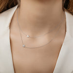 Two dainty white gold necklaces with gold and diamond heart charms layered together.