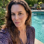 Maya Brenner wearing a freshwater pearl earring charm styled on a gold hoop, paired with layered delicate gold necklaces, in an outdoor setting.