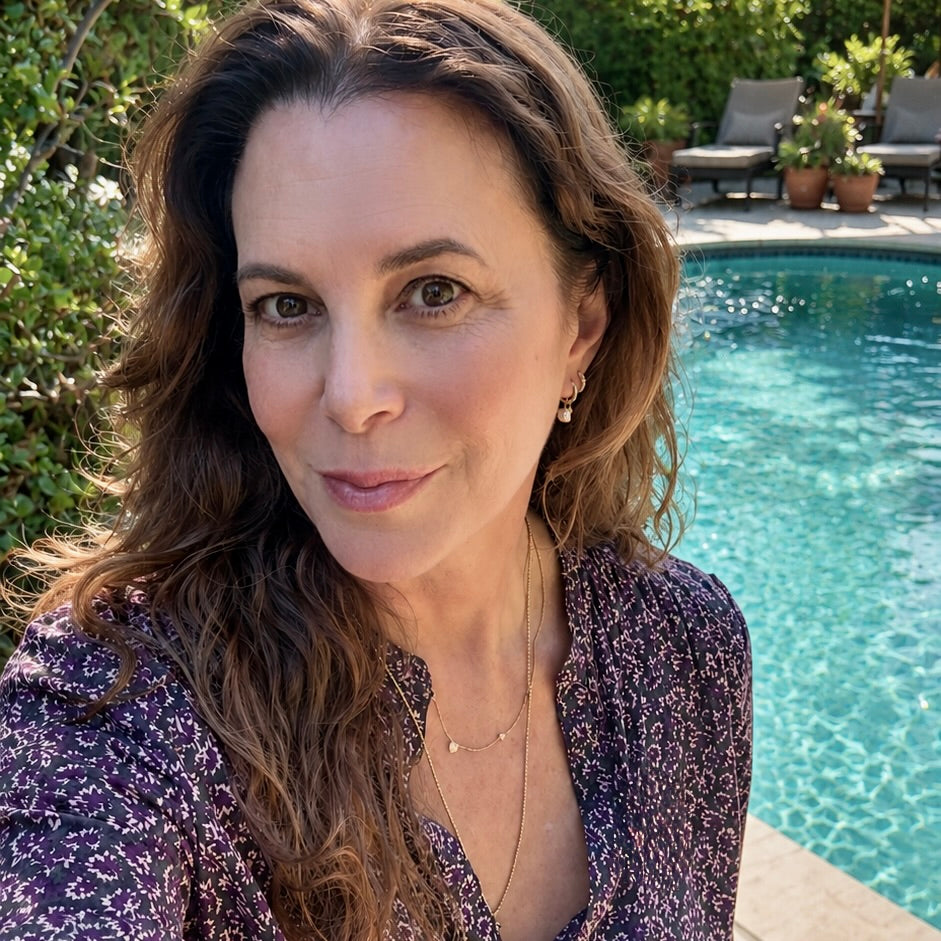 Maya Brenner wearing a freshwater pearl earring charm styled on a gold hoop, paired with layered delicate gold necklaces, in an outdoor setting.