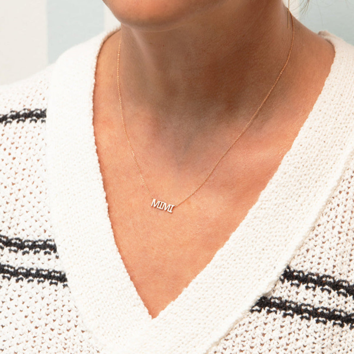 Close-up of a décolletage wearing a MIMI Necklace in rose gold with a cable chain, and a white knit with black horizontal stripes. 