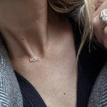 Close-up of a décolletage wearing a Pavé MIMI Necklace, with black and grey knitted clothing and blonde hair visible.