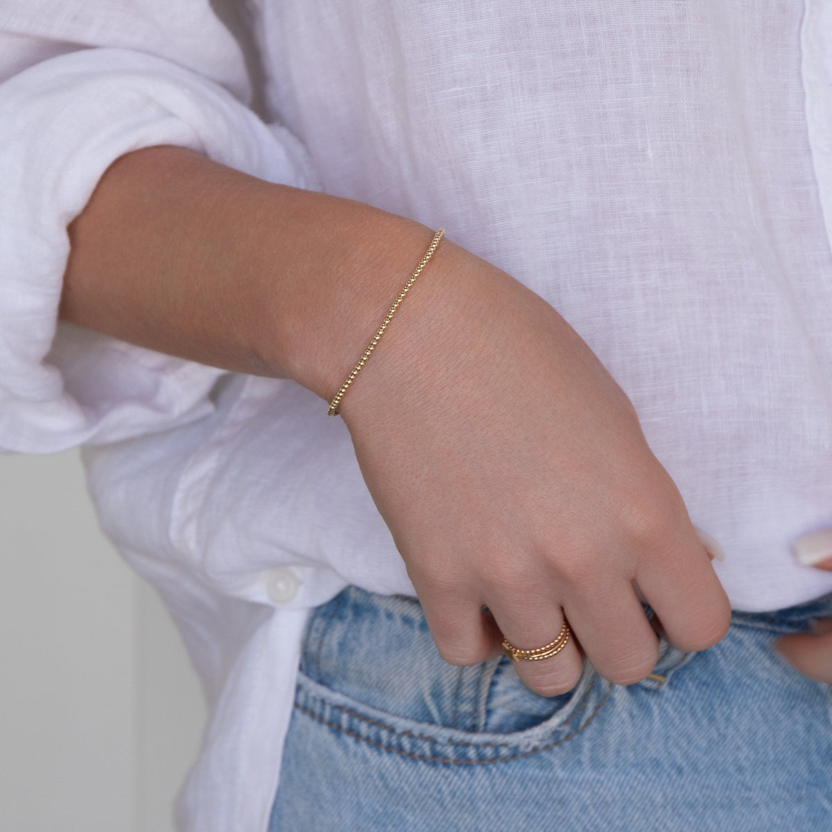 Close-up of a woman’s arm wearing a Mini Bubble Bracelet, two Delicate Beaded Bands and a Twinkle Twinkle Ring, with a white shirt and light blue jeans.