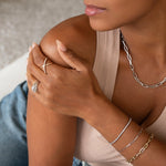 Close-up of a woman wearing mixed metal jewellery in yellow and white gold: a Bold Link Chain, a Bold Link Bracelet, an Element Long Link Bracelet, a Down the Line Bracelet, an Etched Paris Ring and a Criss-Cross Diamond Daze Ring, styled in a nude-coloured top and blue jeans.