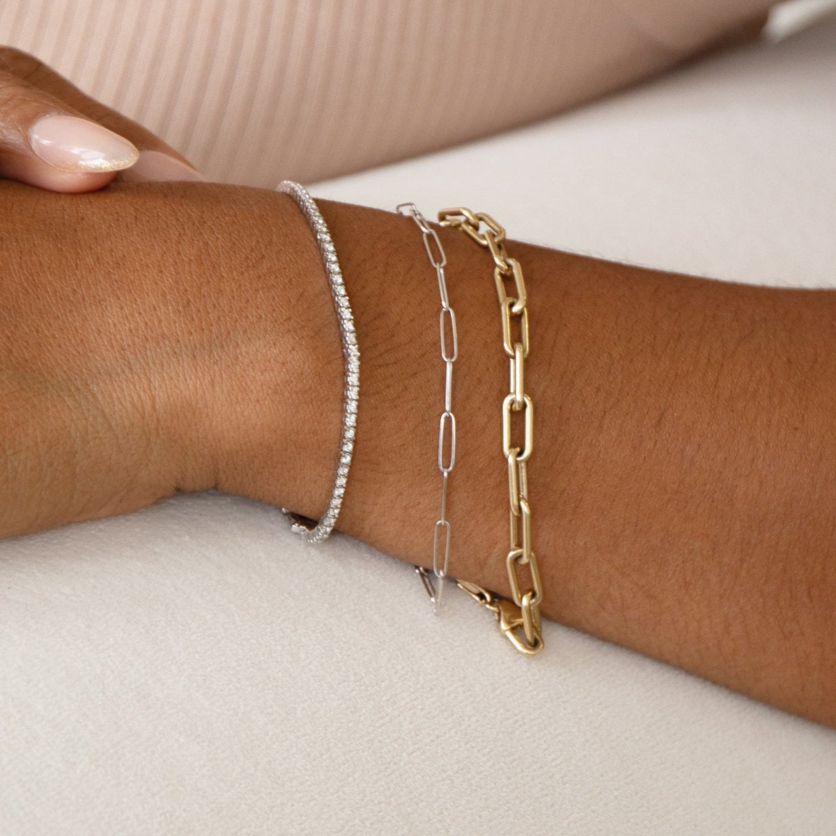 A hand wearing several white gold and yellow gold Love Set Match Bracelets and Down the Line Bracelets, and several yellow gold rings against black background. 