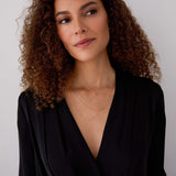 A woman with brown curly hair wearing a black top and three layered Monogram Necklaces with Diamond charms, one in yellow gold with the letter M, one in white gold with the letter R and one in rose gold with the letter J, against a neutral background.