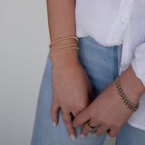 A close-up of a woman's hands wearing mixed metal jewellery, including a Classic Bubble Bracelet, Rolo Bracelets, a Diamond Cut Bracelet, Delicate Beaded Bands and a Thick Band, styled in a white shirt and light blue denim jeans. 