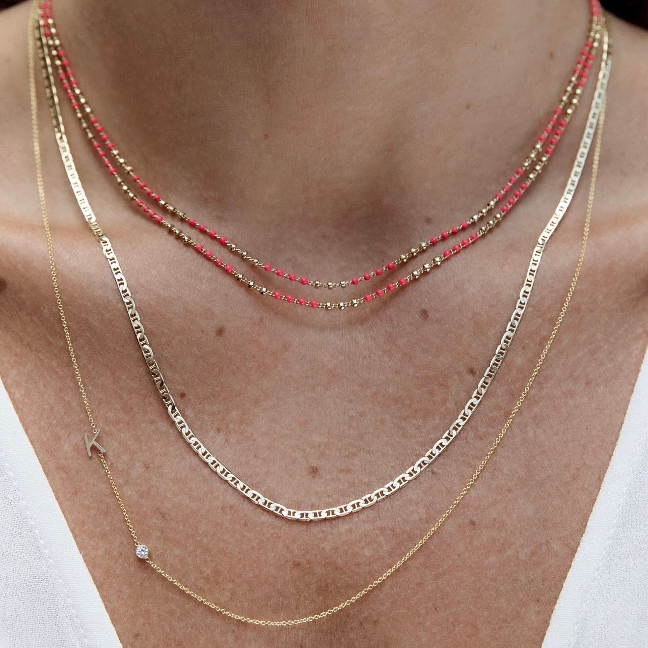 Three necklaces worn on a person's neck with a plain background