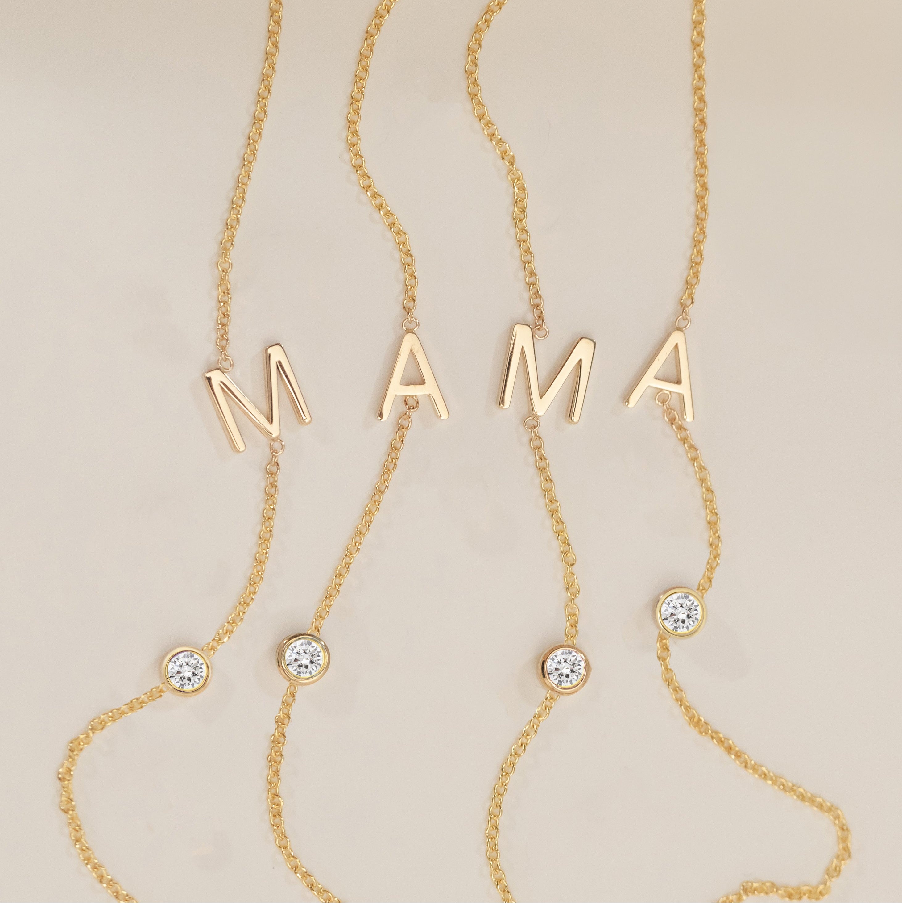 Gold necklace with 'MAMA' letters and small diamonds on a beige background