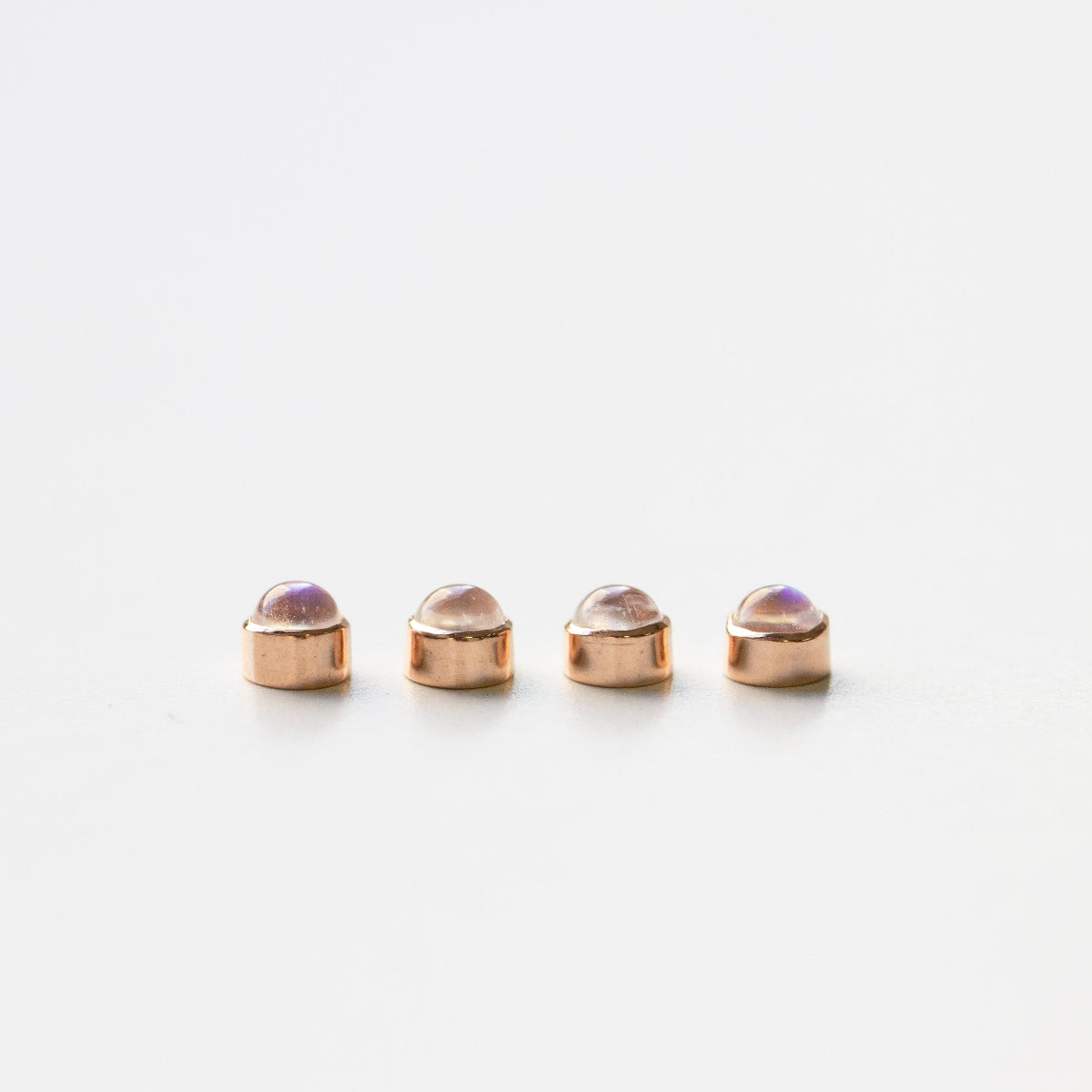 Four rose gold moonstone birthstone charms on a white background. 