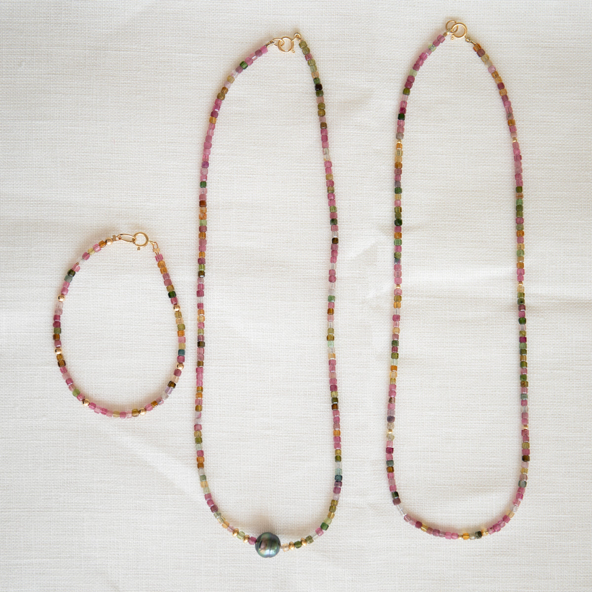 Endless Summer Necklaces in Coral Reef and Sweet Escape and an Endless Summer Bracelet in Coral Reef on a cream fabric background.