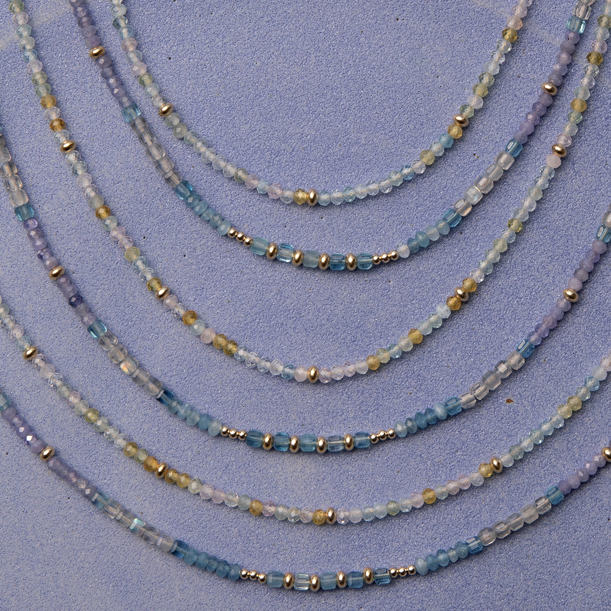 Several Endless Summer Necklaces in Saint-Tropez and Blue Lagoon, laid against a purple background. 