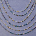 Several Endless Summer Necklaces in Saint-Tropez and Blue Lagoon, laid against a purple background. 
