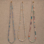 Three Endless Summer Necklaces (Blue Lagoon, Saint-Tropez and Capri) on a beige fabric background. 