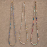 Three Endless Summer Necklaces (Blue Lagoon, Saint-Tropez and Capri) on a beige fabric background. 