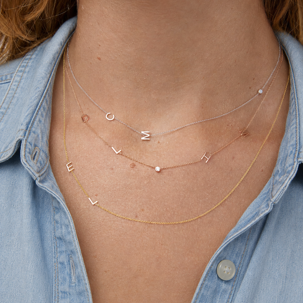 Necklace with letter pendants worn by a person wearing a denim shirt.