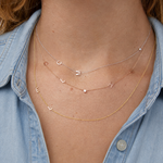 Multiple letter necklaces layered worn by a person wearing a denim shirt.