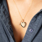 Gold heart-shaped necklace with diamond and pavé diamond 'NANA' pendant on a person wearing a blue shirt.