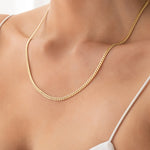 Close-up of a décolletage wearing a Chic Cuban Curb Chain in yellow gold with a white strap top. 