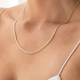 Close-up of a décolletage wearing a Chic Cuban Curb Chain in yellow gold with a white strap top. 