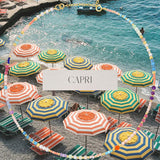 An Endless Summer Necklace - Capri against a beach background with colourful umbrellas and the word 'CAPRI' in the centre. 