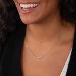 Close-up of a woman's neck wearing a Single Diamond Layering Necklace, a Diamond Arc Layering Necklace and a Custom Gold Necklace - 1 Letter, all in yellow gold, in a black top. 