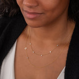 Close-up of a woman's  neck wearing a Quintet Diamond Layering Necklace and a Custom Gold Necklace - 2 Letters with a white top and black cardigan. 