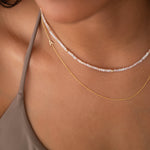 Close-up of a woman's neck wearing an Endless Summer Necklace - Pink Sands and a 14k Asymmetrical Letter Necklace - A, styled in a beige strap top. 