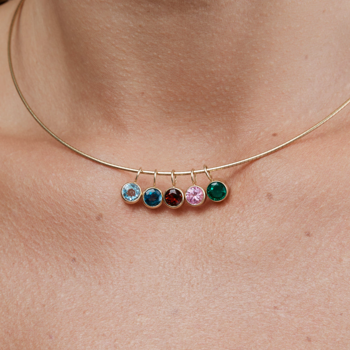 A neck wearing an Omega Chain with Color Pop Pendants in Light Blue (Aquamarine), Blue (London Topaz), Red (Garnet), Light Pink (Pink Tourmaline) and Green (Lab Grown Emerald). 