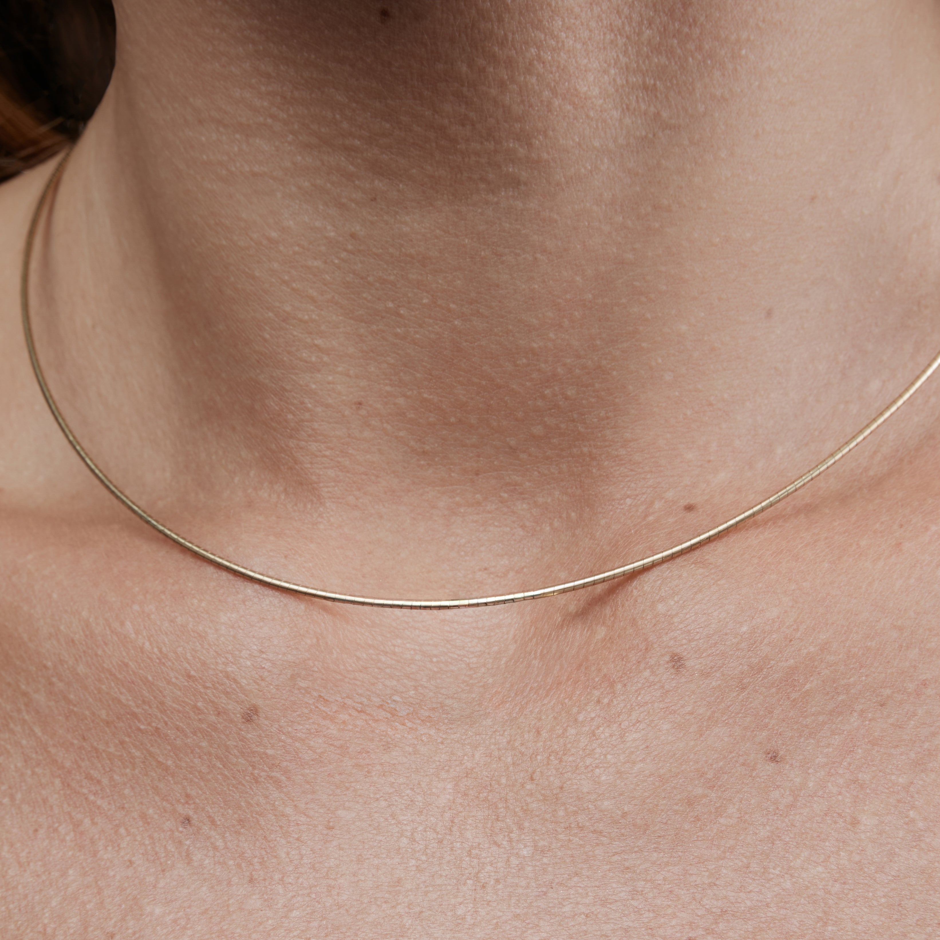 Close-up of a thin gold necklace on a person's neck