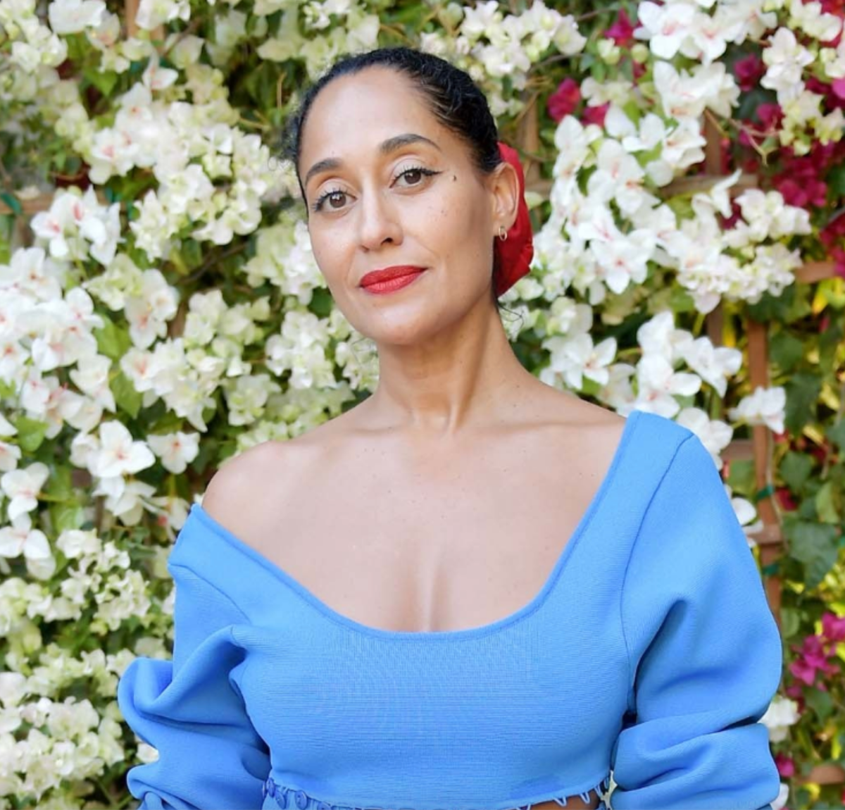 A woman wearing an Open Eclipse Earring - Small in yellow gold with a blue top and red lipstick against a floral background. 
