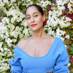 A woman wearing an Open Eclipse Earring - Small in yellow gold with a blue top and red lipstick against a floral background. 