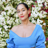 A woman wearing an Open Eclipse Earring - Small in yellow gold with a blue top and red lipstick against a floral background. 