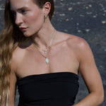 Woman wearing a black strapless top wearing the Etched Paris Earring and  layered gold charm necklaces against a dark background.