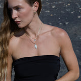 Woman wearing a black strapless top wearing the Etched Paris Earring and  layered gold charm necklaces against a dark background.
