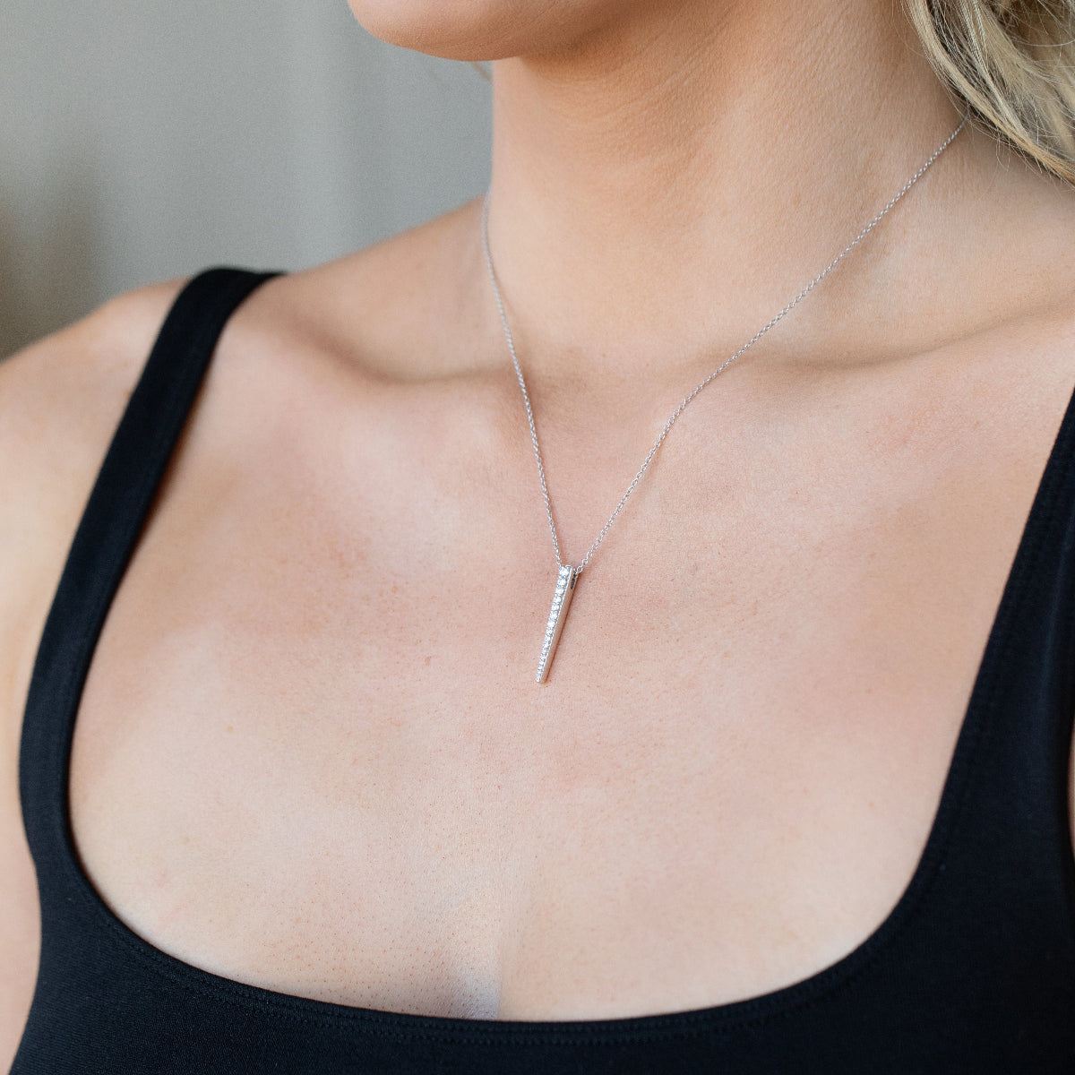A close-up of a blonde woman's décolletage wearing a Love Struck Diamond Necklace in white gold, styled in a black top. 
